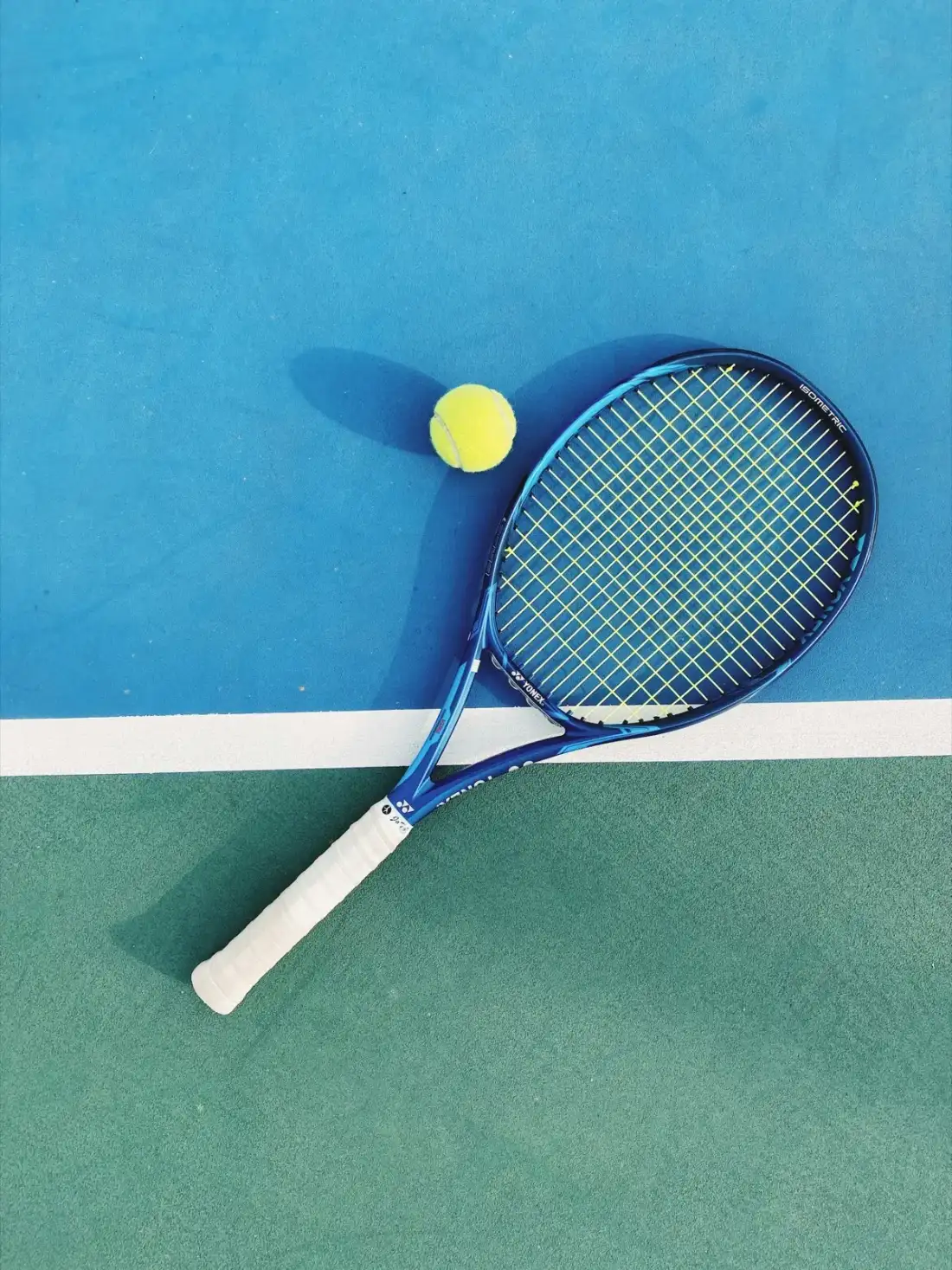 Raquete de tênis azul e bola sobre uma quadra rápida
